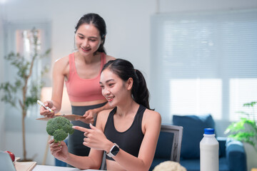 Asian nutritionist holding clipboard is coaching a young woman about healthy food and explaining benefits of eating broccoli, during a consultation