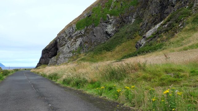 Snib's Cave or Bennane Cave by disused abandoned road, cone shape Alsa island in Irish Sea, panning left.