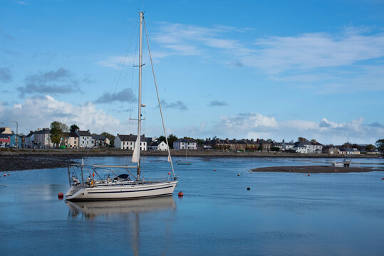 A serene coastal village harbor with a sailboat anchored in calm waters, under clear sky. Picturesque houses line shore, creating a peaceful idyllic scene. Not season for vacatio on a yacht