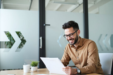 Fototapeta premium Man sitting at desk working on laptop and paper, focused and modern