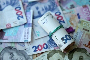 Roll of 500 Ukrainian Hryvnia money bills lies on big pile of ukrainian currency money close up