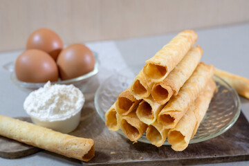 A stack of freshly baked Egg Roll cookies or biscuits displayed with flour and eggs, highlighting homemade baking with simple ingredients. Perfect for a cozy dessert or snack idea.