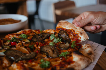 Hand holds an appetizing slice of vegetable pizza with parsley. Delicious, freshly made pizza with a crispy crust