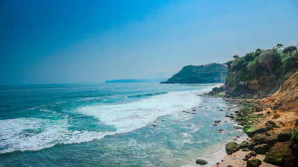 Beautiful beach with blue sky and green cliffs.