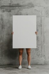 Person holding a large blank poster against a concrete wall