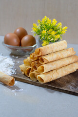 A stack of freshly baked Egg Roll cookies or biscuits displayed with flour and eggs, highlighting homemade baking with simple ingredients. Perfect for a cozy dessert or snack idea.