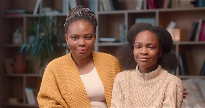 Portrait of beautiful African American women looking at each other and posing for camera. Mother and daughter spending time together. Cute female hugging girl at library. Family concept.