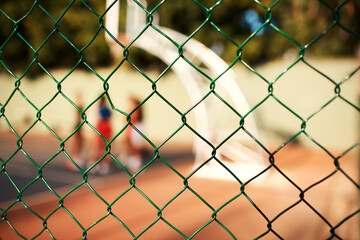 Fototapeta premium Fence, basketball court and safety with steel for game, match or blur background of outdoor turf. Closeup, security and boundry with people, team or netting for sport, yard or boundary gate on pitch