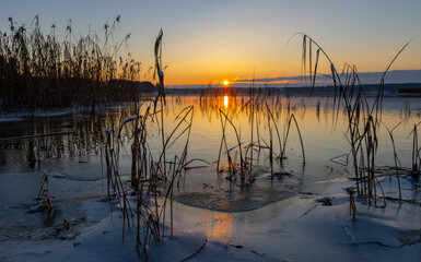 A wonderful view of a lake frozen by the shore at sunset. Great colorful sky with sun. Latvia. Baltezers