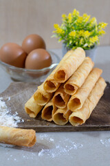 A stack of freshly baked Egg Roll cookies or biscuits displayed with flour and eggs, highlighting homemade baking with simple ingredients. Perfect for a cozy dessert or snack idea.