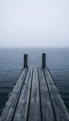 Obraz premium A wooden pier extends out into a foggy lake, disappearing into the mist.