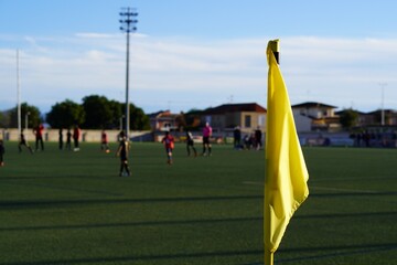 yellow corner flag on a soccer field in a children's soccer game, with players and referee in the...