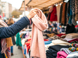 Fototapeta premium Close-Up of a Hand Browsing Vintage Clothing at a Flea Market, Exploring Textures and Colors of Secondhand Fashion