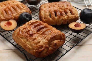 Delicious puff pastries and plums on white wooden table, closeup