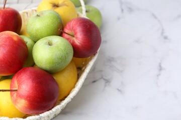 Different ripe apples in basket on white table, closeup. Space for text