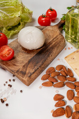 Large ball of Italian mozzarella di Bufala Campana on a chopping board with tomatoes, lettuce leaves, nuts and other ingredients for making salad.