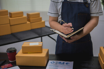 An Asian man carefully prepares a package for a customer's online order, methodically placing items...