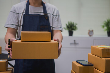 An Asian man carefully prepares a package for a customer's online order, methodically placing items...