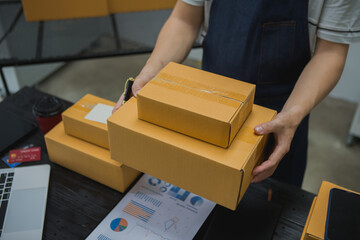 An Asian man carefully prepares a package for a customer's online order, methodically placing items in a box, sealing it securely, and attaching a shipping label for prompt delivery.