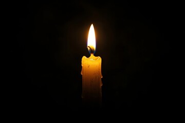 Burning candle with melting wax illuminating the darkness
