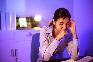 Asian woman diligently works overtime, managing a heavy workload with focus and determination....