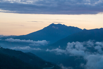 Breathtaking dawn view of mountains shrouded in clouds over a serene landscape at sunrise in tranquil surroundings