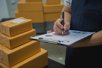 An Asian man carefully prepares a package for a customer's online order, methodically placing items in a box, sealing it securely, and attaching a shipping label for prompt delivery.