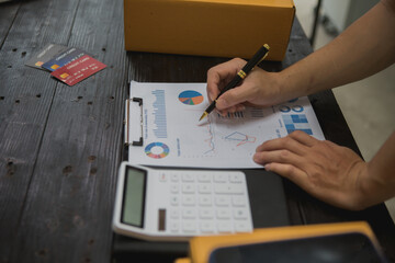 An Asian man carefully prepares a package for a customer's online order, methodically placing items in a box, sealing it securely, and attaching a shipping label for prompt delivery.