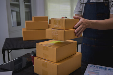 An Asian man carefully prepares a package for a customer's online order, methodically placing items...