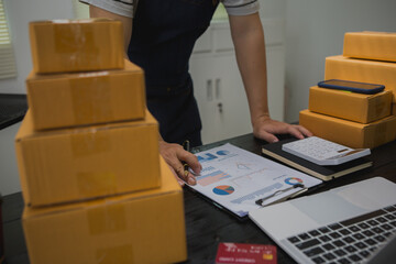 An Asian man carefully prepares a package for a customer's online order, methodically placing items...