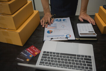 An Asian man carefully prepares a package for a customer's online order, methodically placing items...