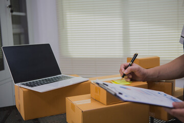 An Asian man carefully prepares a package for a customer's online order, methodically placing items in a box, sealing it securely, and attaching a shipping label for prompt delivery.