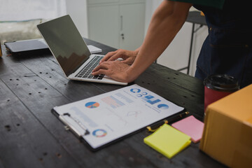 An Asian man carefully prepares a package for a customer's online order, methodically placing items in a box, sealing it securely, and attaching a shipping label for prompt delivery.