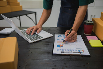An Asian man carefully prepares a package for a customer's online order, methodically placing items...
