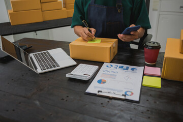 An Asian man carefully prepares a package for a customer's online order, methodically placing items...