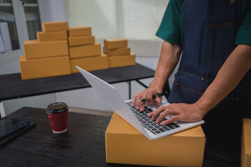 An Asian man carefully prepares a package for a customer's online order, methodically placing items...