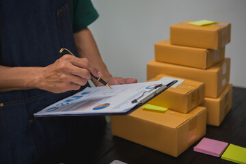 An Asian man carefully prepares a package for a customer's online order, methodically placing items in a box, sealing it securely, and attaching a shipping label for prompt delivery.