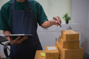 An Asian man carefully prepares a package for a customer's online order, methodically placing items...
