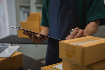 An Asian man carefully prepares a package for a customer's online order, methodically placing items in a box, sealing it securely, and attaching a shipping label for prompt delivery.