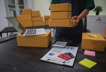 An Asian man carefully prepares a package for a customer's online order, methodically placing items...
