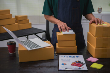 An Asian man carefully prepares a package for a customer's online order, methodically placing items...