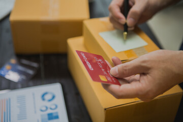 An Asian man carefully prepares a package for a customer's online order, methodically placing items in a box, sealing it securely, and attaching a shipping label for prompt delivery.
