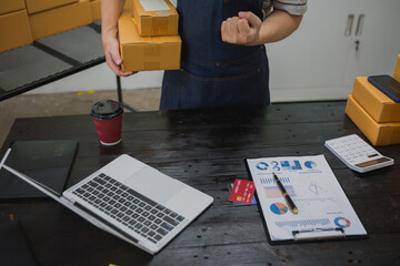 An Asian man carefully prepares a package for a customer's online order, methodically placing items...
