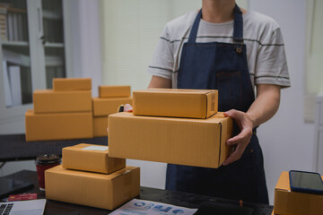 An Asian man carefully prepares a package for a customer's online order, methodically placing items in a box, sealing it securely, and attaching a shipping label for prompt delivery.