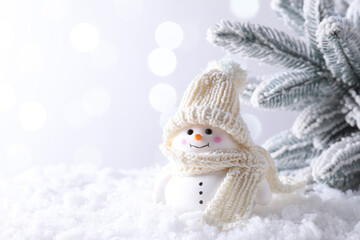 Cute decorative snowman on artificial snow against light background, space for text