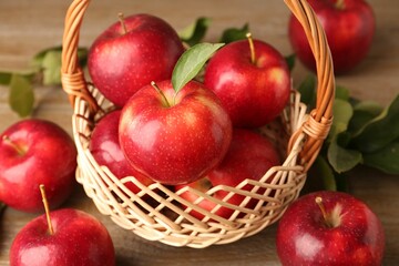 Fresh ripe red apples in wicker basket on wooden table, closeup