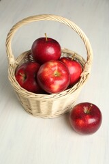 Fresh ripe red apples in wicker basket on white wooden table