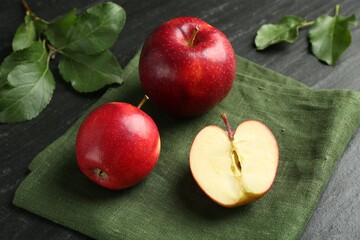 Whole and cut ripe red apples with green leaves on grey textured table