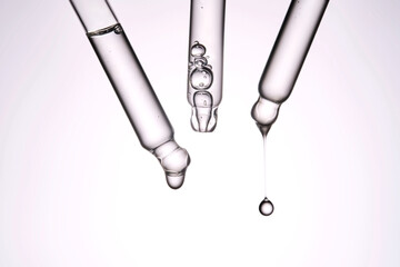 Three pipettes with a cosmetic product. Serum or fluid drips from one of them.