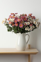 Vase with beautiful flowers on wooden shelf near white wall